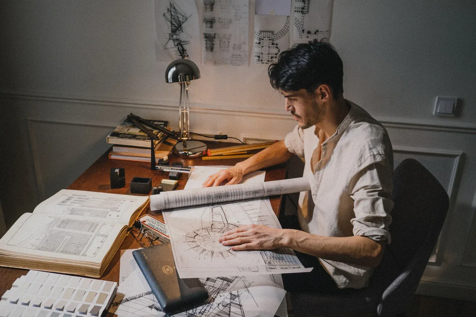 Engineer working through technical drawings and a rolled blueprint under a work lamp, the documentation stage behind an ODM downlight cut-out specification