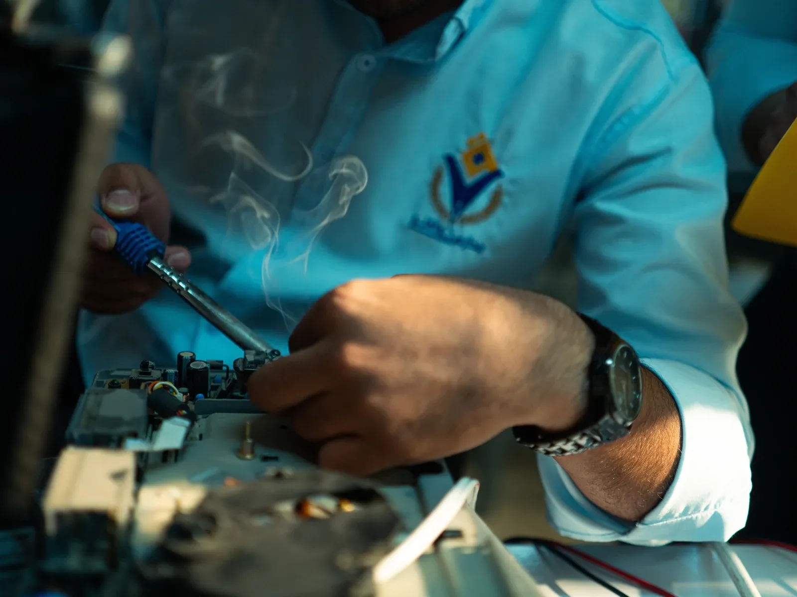 Close-up of a technician assembling and soldering an LED light engine on a sample bench, the light-engine stage of a recessed downlight build