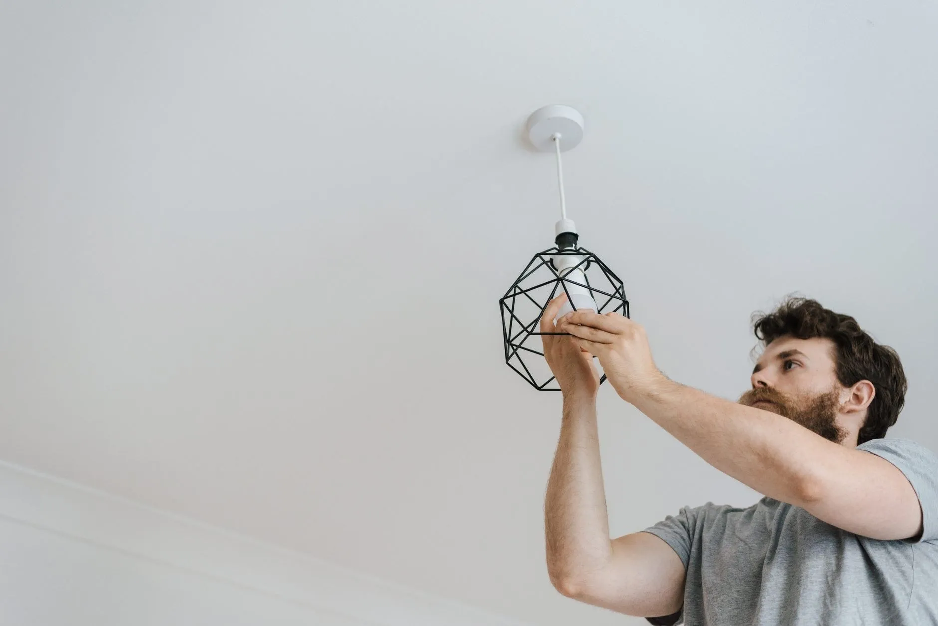 Electrician installing a pendant luminaire on site to a commercial fit-out schedule, illustrating the installation stage of a lighting project