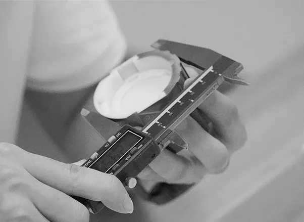 ENCORE QC technician measuring a finished downlight component with digital calipers at an inspection bench, checking the dimensional gate before packing