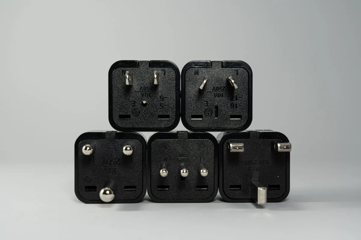 Collection of international black power plug adapters stacked on a grey surface showing different national pin standards