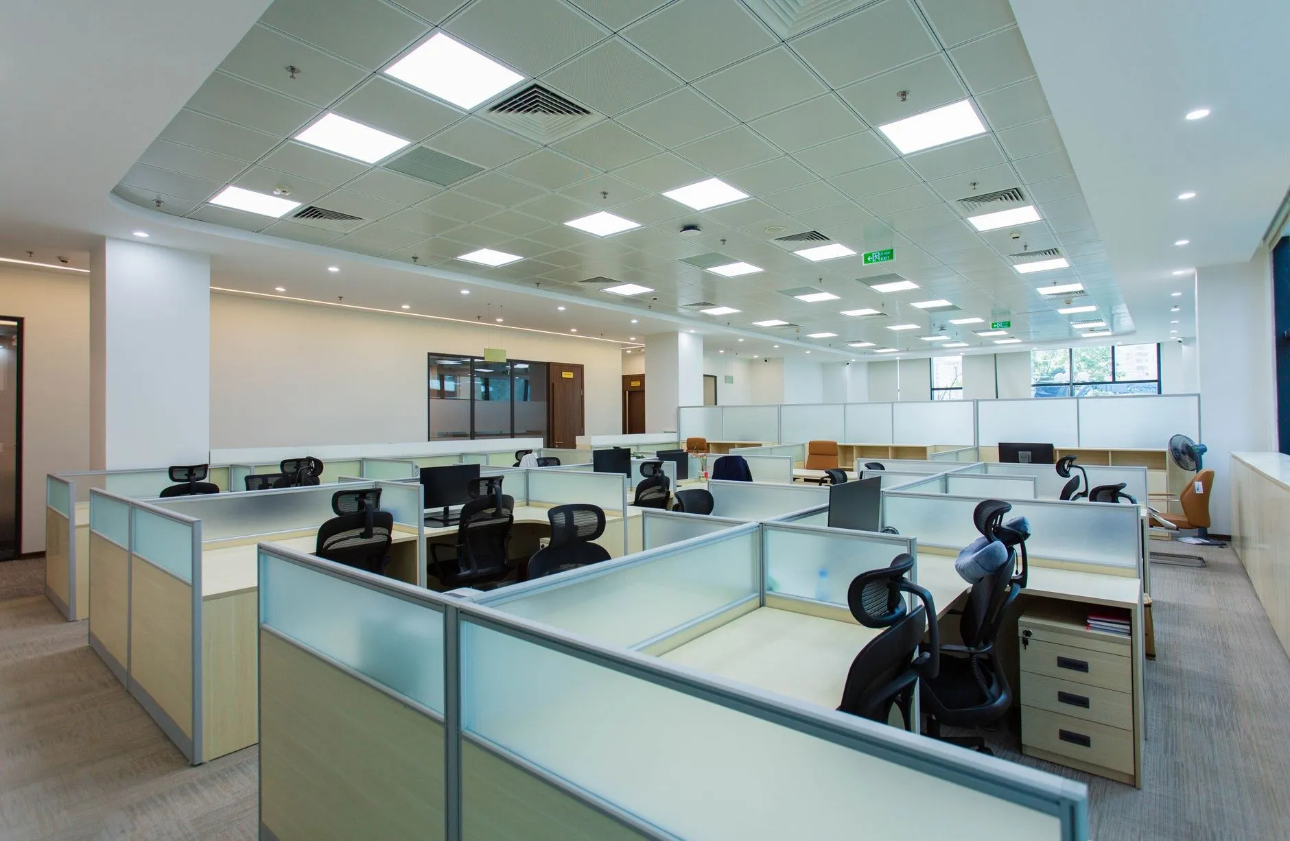 Open-plan office ceiling with recessed LED panel lighting and glazed partitions, a typical commercial office lighting specification