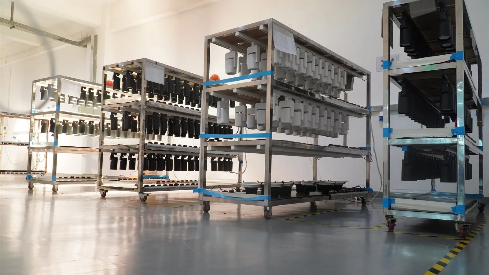 LED lighting quality control — rows of finished LED track lights running on an aging test rack in a clean, modern lighting factory