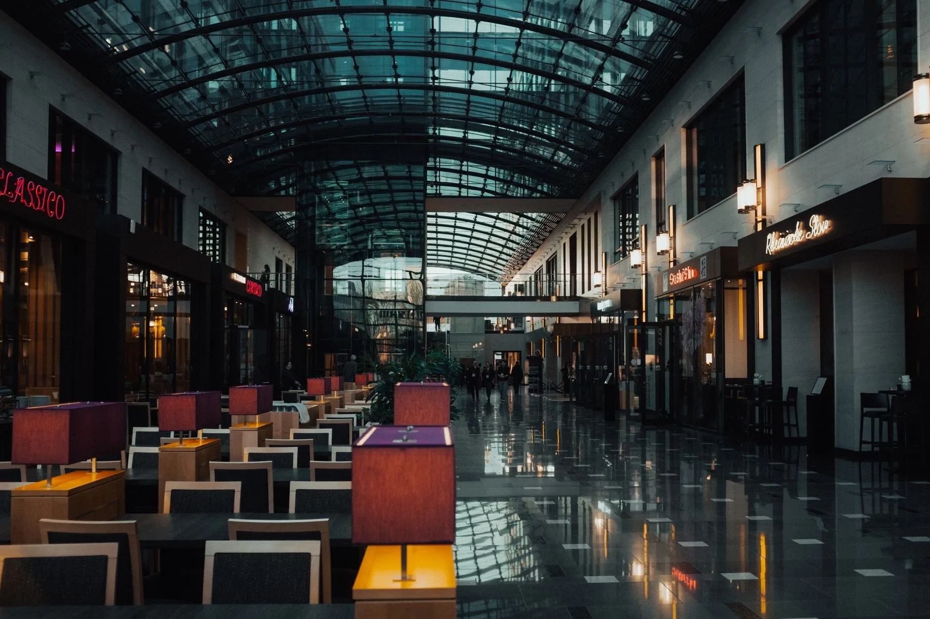 Glass-roofed retail arcade at dusk with commercial spotlights washing the stone floor, an example of retail commercial lighting delivered as a project package