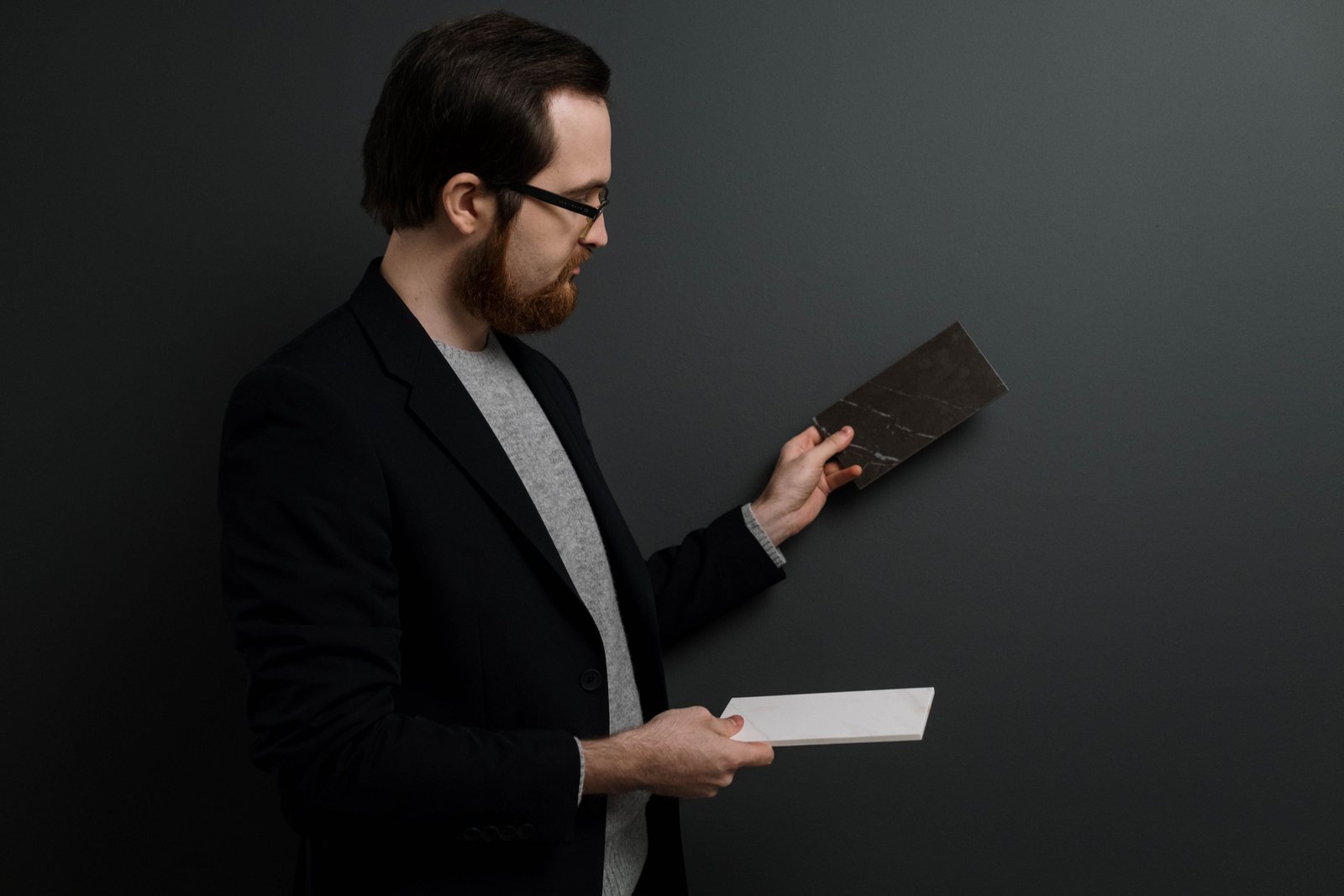 A designer comparing two material samples in hand against a dark wall, deciding between finishes