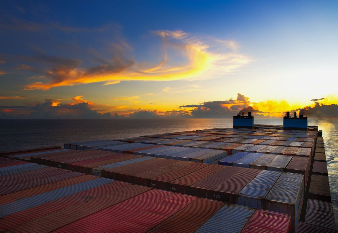 A container ship loaded with containers crossing open water at sunset — the last stage of the LED lighting supply chain